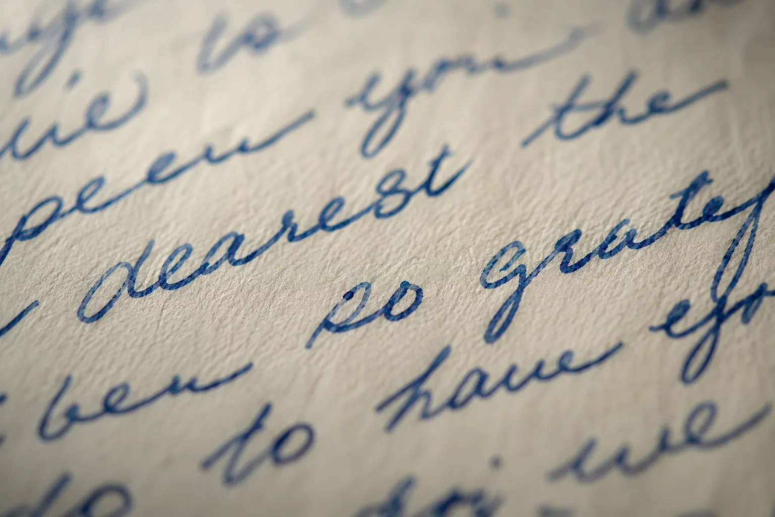 Hands unfolding a blue-ink handwritten letter on a worn oak table, a phone beside it